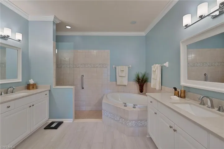 Full bath featuring two vanities, a shower stall, a bath, ornamental molding, and recessed lighting