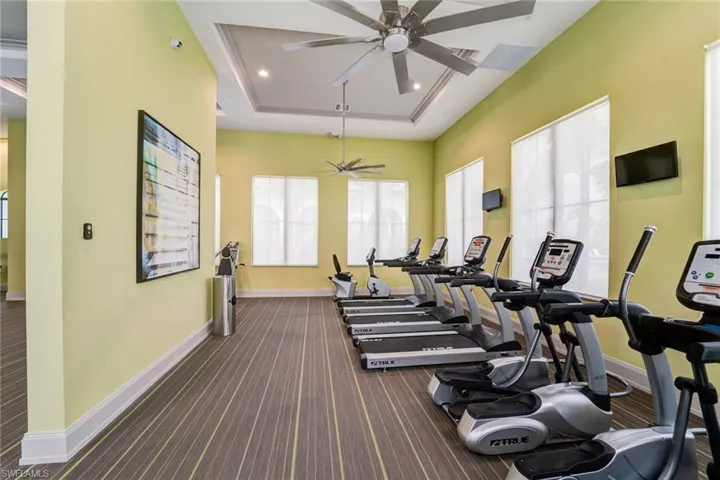 Exercise room featuring dark carpet, a raised ceiling, and ceiling fan