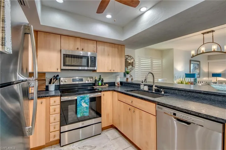Kitchen featuring light brown cabinets, sink, ceiling fan with notable chandelier, and stainless steel appliances