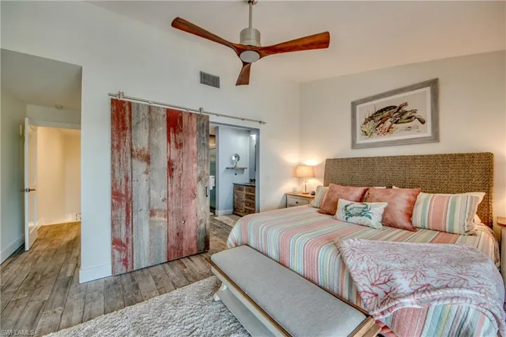Bedroom with ensuite bath, a barn door, ceiling fan, and hardwood / wood-style flooring