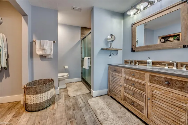 Bathroom featuring oversized vanity, dual sinks, hardwood / wood-style flooring, toilet, and a shower with shower door