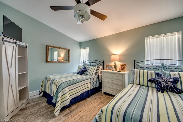Bedroom with a barn door, ceiling fan, vaulted ceiling, and light hardwood / wood-style floors