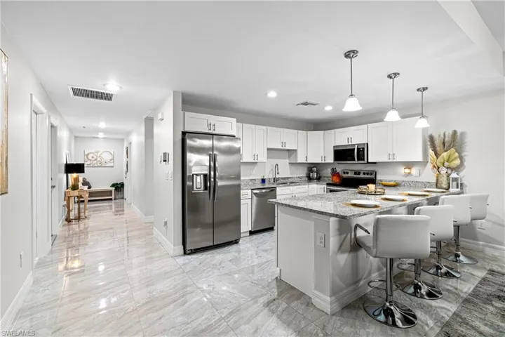 Kitchen with stainless steel appliances, a peninsula, pendant lighting, light stone counters, and a kitchen bar