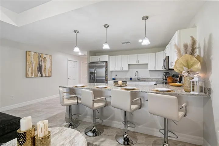 Kitchen with a peninsula, light stone counters, white cabinetry, a kitchen breakfast bar, and pendant lighting