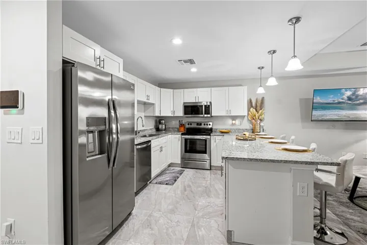 Kitchen featuring appliances with stainless steel finishes, a kitchen breakfast bar, light stone countertops, white cabinetry, and decorative light fixtures