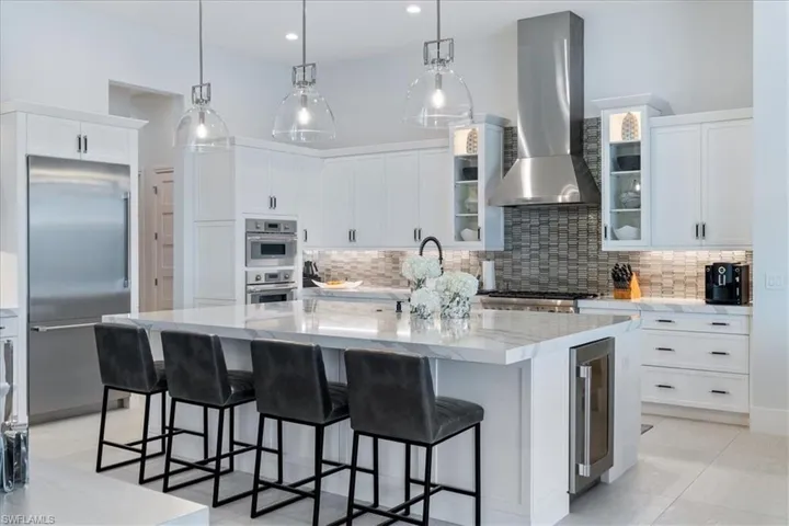 Kitchen featuring decorative backsplash, stainless steel appliances, beverage cooler, wall chimney range hood, and a large island with sink