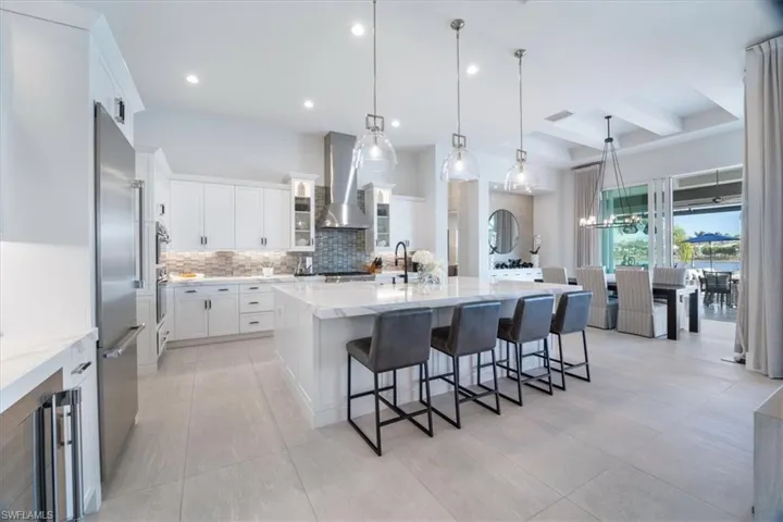 Kitchen featuring a kitchen breakfast bar, a spacious island, wall chimney range hood, hanging light fixtures, and white cabinetry