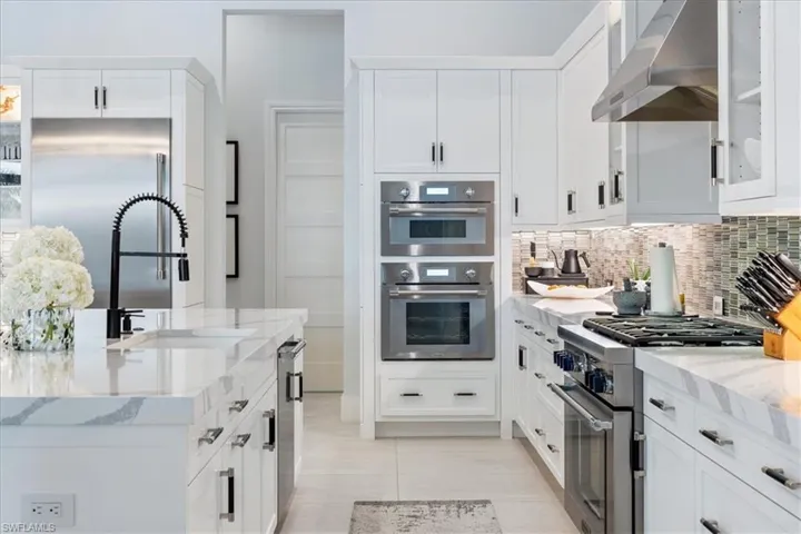 Kitchen with decorative backsplash, white cabinetry, high end appliances, and wall chimney range hood