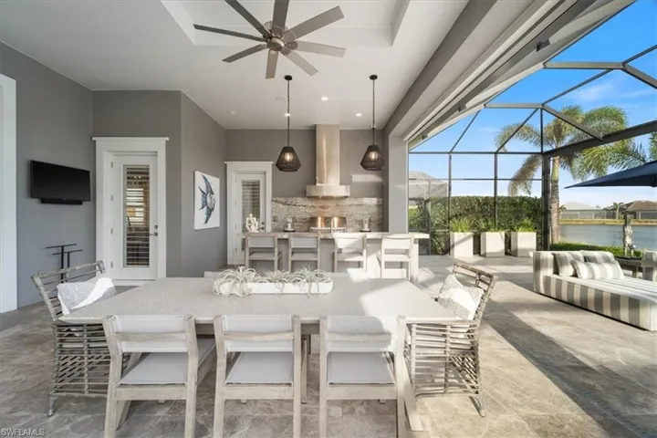 View of patio featuring exterior bar, a water view, glass enclosure, and ceiling fan