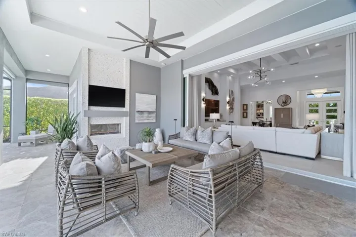Living room with ceiling fan with notable chandelier, a healthy amount of sunlight, beam ceiling, and a fireplace