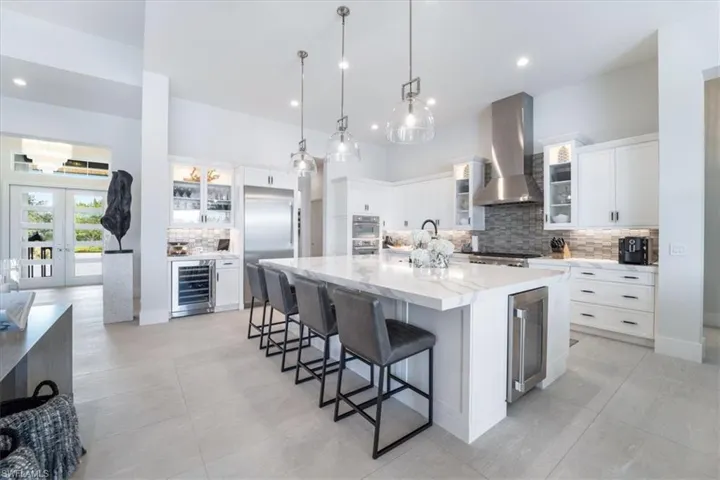 Kitchen with a spacious island, white cabinetry, wall chimney exhaust hood, and beverage cooler