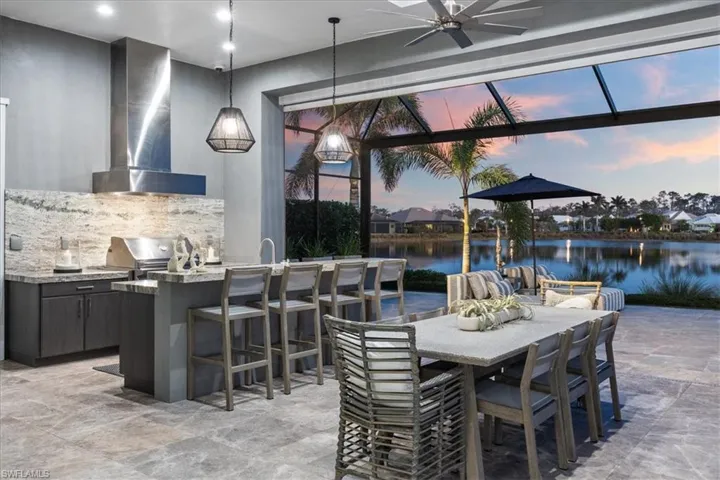 Patio terrace at dusk with grilling area, a water view, ceiling fan, a bar, and exterior kitchen