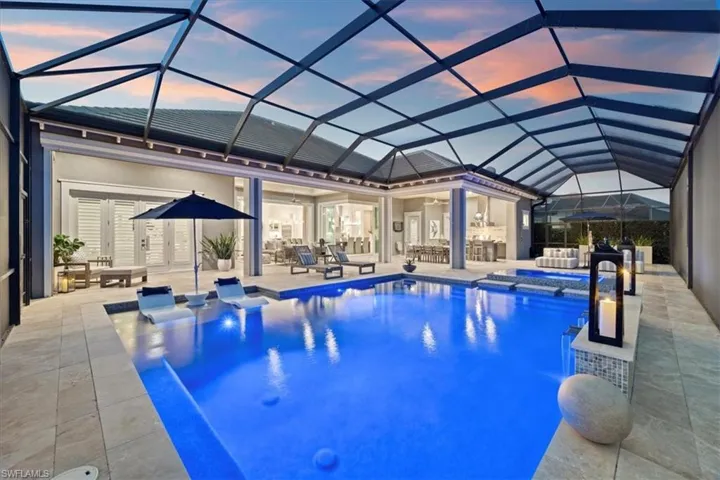 Pool at dusk featuring an in ground hot tub, a patio, and glass enclosure