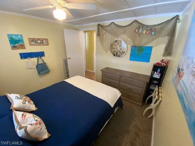 Bedroom featuring ceiling fan, dark carpet, and ornamental molding