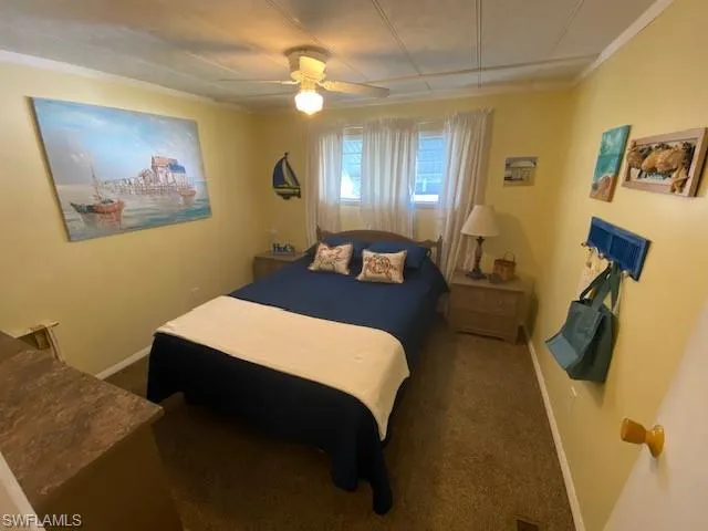 Bedroom with a ceiling fan, dark carpet, and crown molding