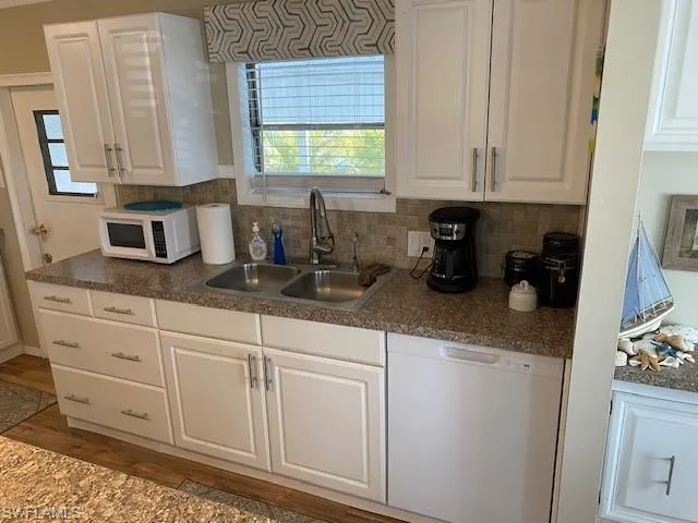 Kitchen with white appliances, white cabinetry, dark countertops, backsplash, and dark wood-style flooring
