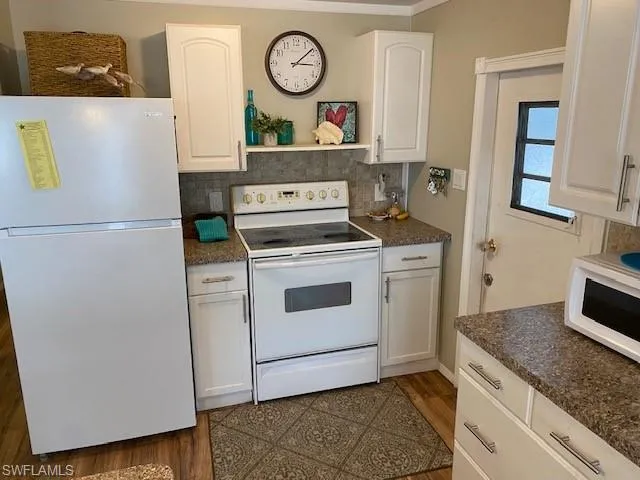 Kitchen with dark countertops, white appliances, and white cabinets