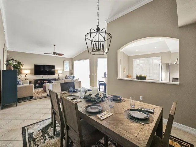 Dining area featuring crown molding, light tile patterned floors, lofted ceiling, a ceiling fan, and a chandelier