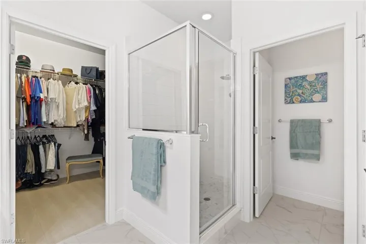 Full bathroom featuring a stall shower, a spacious closet, and light marble finish floors