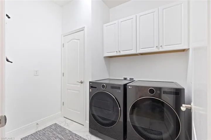 Laundry area with washer and clothes dryer, light marble finish floors, and cabinet space