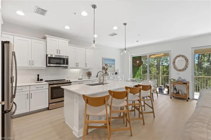 Kitchen with stainless steel appliances, a kitchen bar, pendant lighting, white cabinetry, and an island with sink