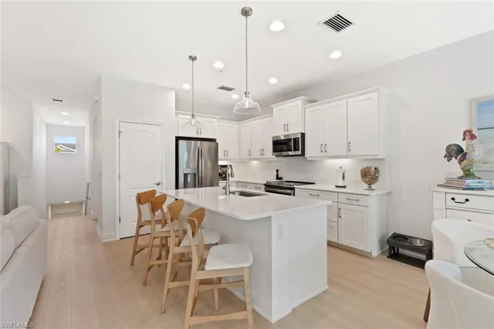 Kitchen featuring open floor plan, appliances with stainless steel finishes, a kitchen bar, white cabinets, and light wood finished floors