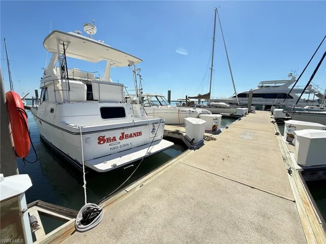 Dockside property featuring a concrete pier with multiple mooring cleats, a white motor yacht, and surrounding water access