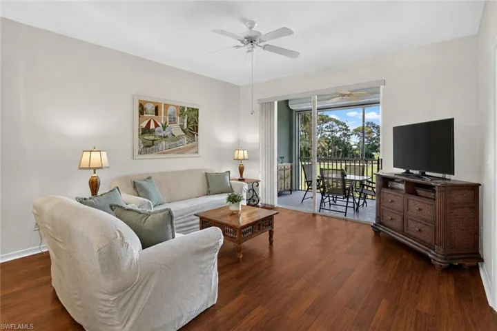 Open-concept living area featuring wood-finish flooring, a ceiling fan, and a screened lanai with outdoor seating