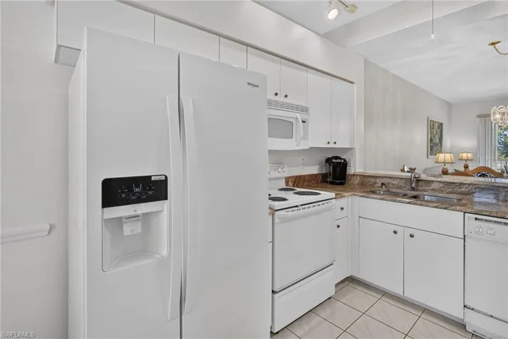 Kitchen featuring white appliances, upper and lower cabinetry, a double basin sink, and a stone countertop