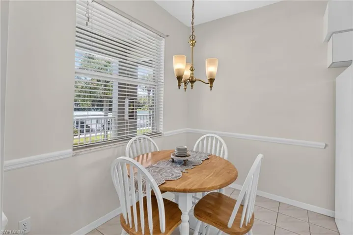 Dining area featuring a brass chandelier with frosted glass shades, a large window with horizontal blinds, decorative chair rail molding, and neutral wall paint