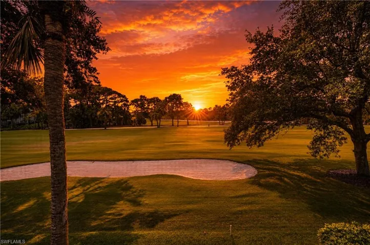 Expansive green golf course featuring a sand trap, mature trees, and a palm tree