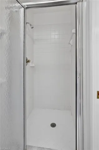 Shower enclosure featuring white tile walls and floor, a chrome showerhead, and a translucent framed glass door