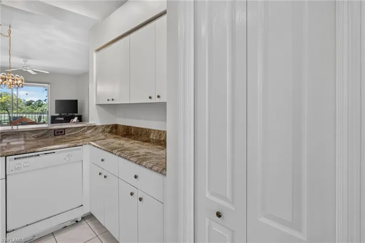 Kitchen area featuring white cabinetry, integrated white dishwasher, and stone countertops extending to a breakfast bar