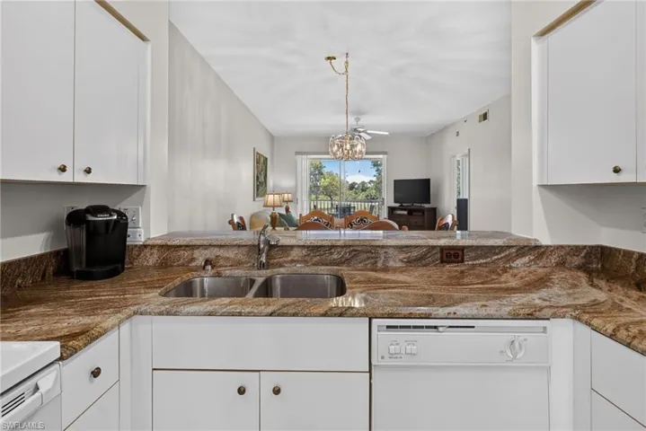 Kitchen featuring extensive stone countertops, white cabinetry with round hardware, double stainless steel sink, and integrated white dishwasher