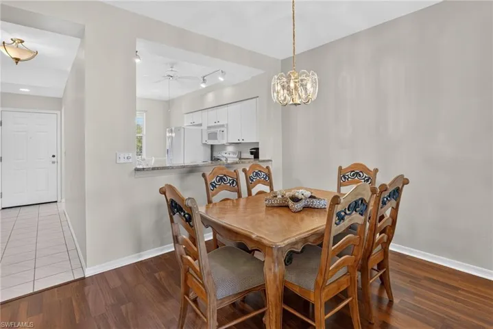 Dining area featuring wood-finish flooring and a decorative chandelier, with a pass-through opening to a kitchen with white cabinetry and appliances