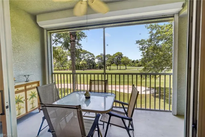 Screened patio with textured walls and a ceiling fan, featuring a golf course backdrop with sand traps and mature trees