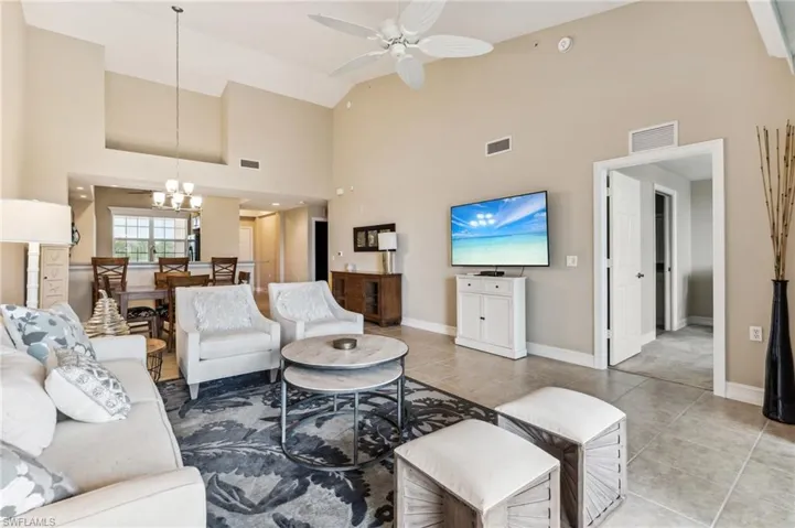Living room featuring ceiling fan with notable chandelier, light tile patterned floors, and high vaulted ceiling