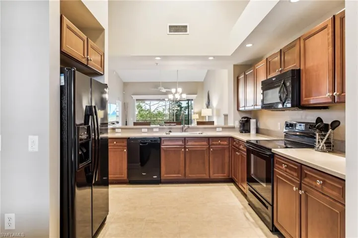 Kitchen with sink, a notable chandelier, kitchen peninsula, black appliances, and light tile patterned floors