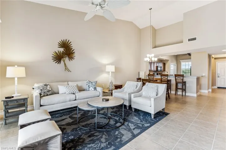 Living room with ceiling fan with notable chandelier, high vaulted ceiling, and light tile patterned floors