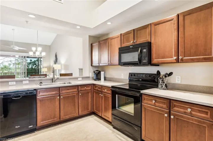 Kitchen featuring light tile patterned flooring, lofted ceiling, sink, black appliances, and an inviting chandelier