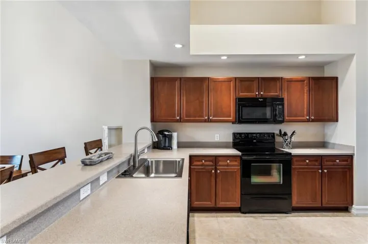 Kitchen with black appliances, a kitchen bar, light tile patterned floors, and sink