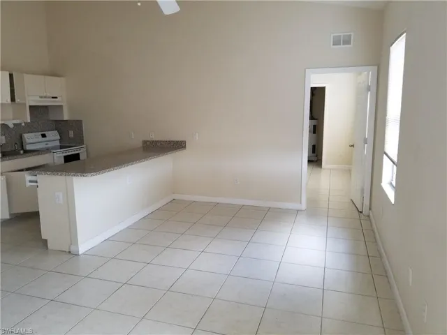 Kitchen with a peninsula, white cabinets, white range with electric stovetop, decorative backsplash, and light tile patterned floors