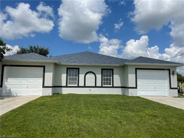 Ranch-style home with a front yard, an attached garage, and stucco siding