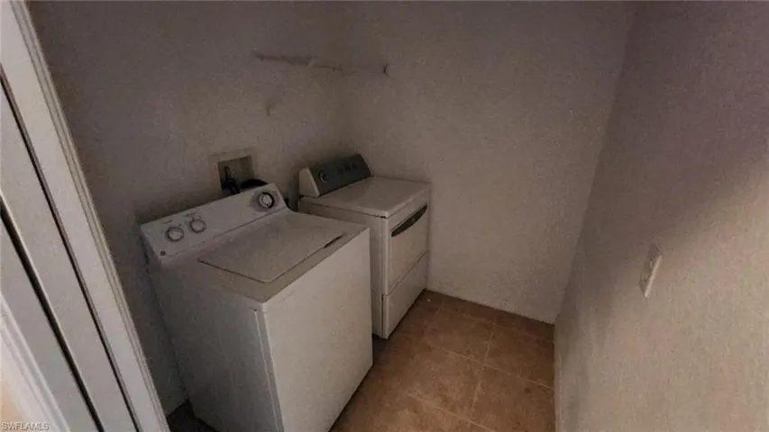 Clothes washing area with light tile patterned flooring and washer and dryer