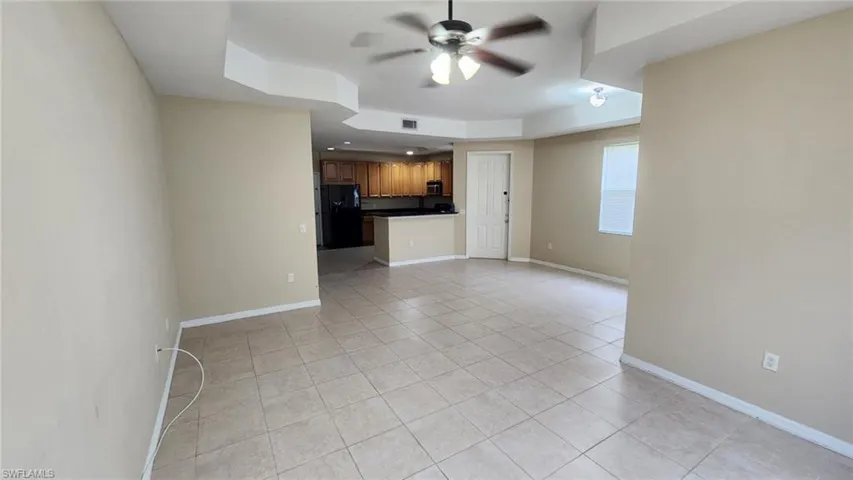Unfurnished room with a tray ceiling, light tile patterned floors, and ceiling fan