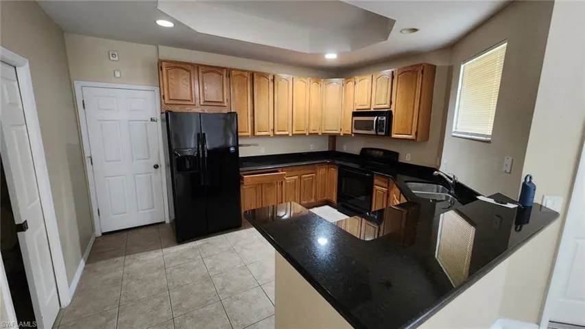 Kitchen featuring black appliances, sink, kitchen peninsula, light tile patterned flooring, and a raised ceiling