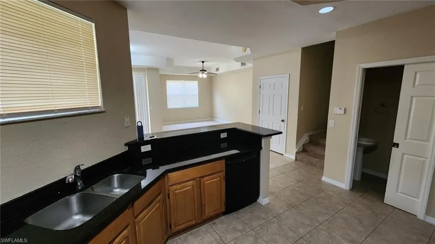 Kitchen with black dishwasher, sink, light tile patterned floors, and ceiling fan