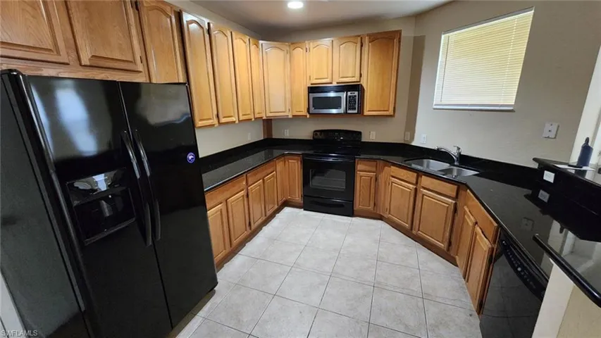 Kitchen with dark stone countertops, black appliances, sink, and light tile patterned floors