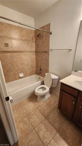 Full bathroom with vanity, tiled shower / bath combo, toilet, and tile patterned floors