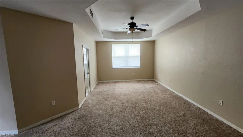 Carpeted empty room featuring a textured ceiling, ceiling fan, and a raised ceiling